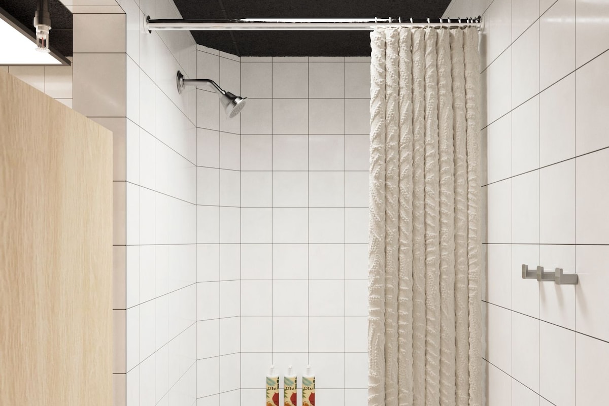 A modern shower area with white tiles, a grey floor, and a wooden door.
