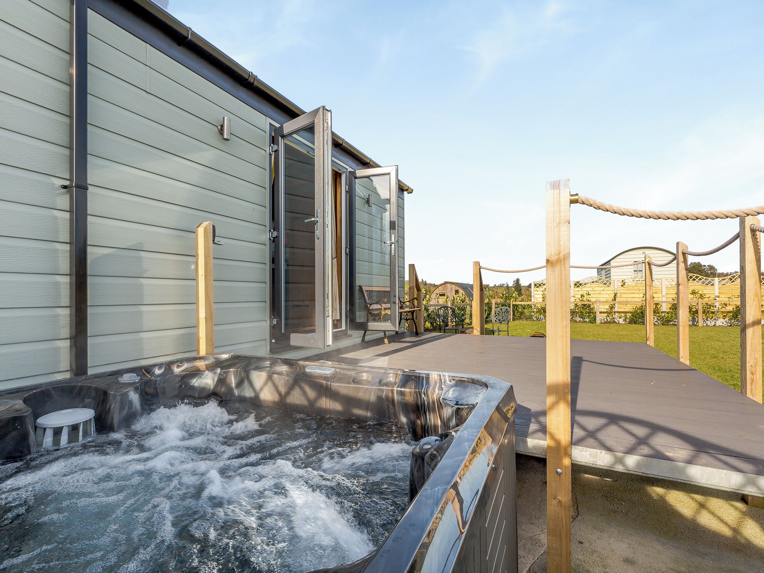 Un espace de bien-être comprenant un jacuzzi, une terrasse en bois et l’entrée du bâtiment.