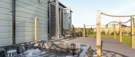 A spa area with a hot tub, wooden deck, and a building entrance.