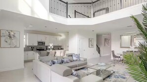 A spacious, modern living area with a large sectional sofa, a glass coffee table, and a kitchen in the background. - Spacious 5Bdr 5Bth ChampionsGate Villa Near Disney, Private Pool & Resort Access (Davenport)