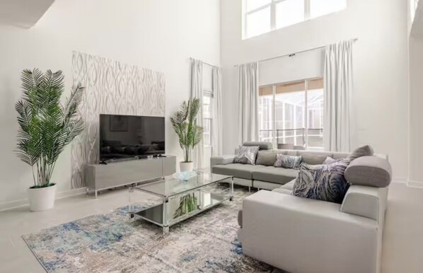 Un salón moderno con un sofá, una mesa de centro y un televisor. Hay dos plantas en macetas y una pared con diseño.