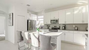 A modern kitchen with white cabinetry, stainless steel appliances, and a central island with bar stools. - Spacious 5Bdr 5Bth ChampionsGate Villa Near Disney, Private Pool & Resort Access (Davenport)