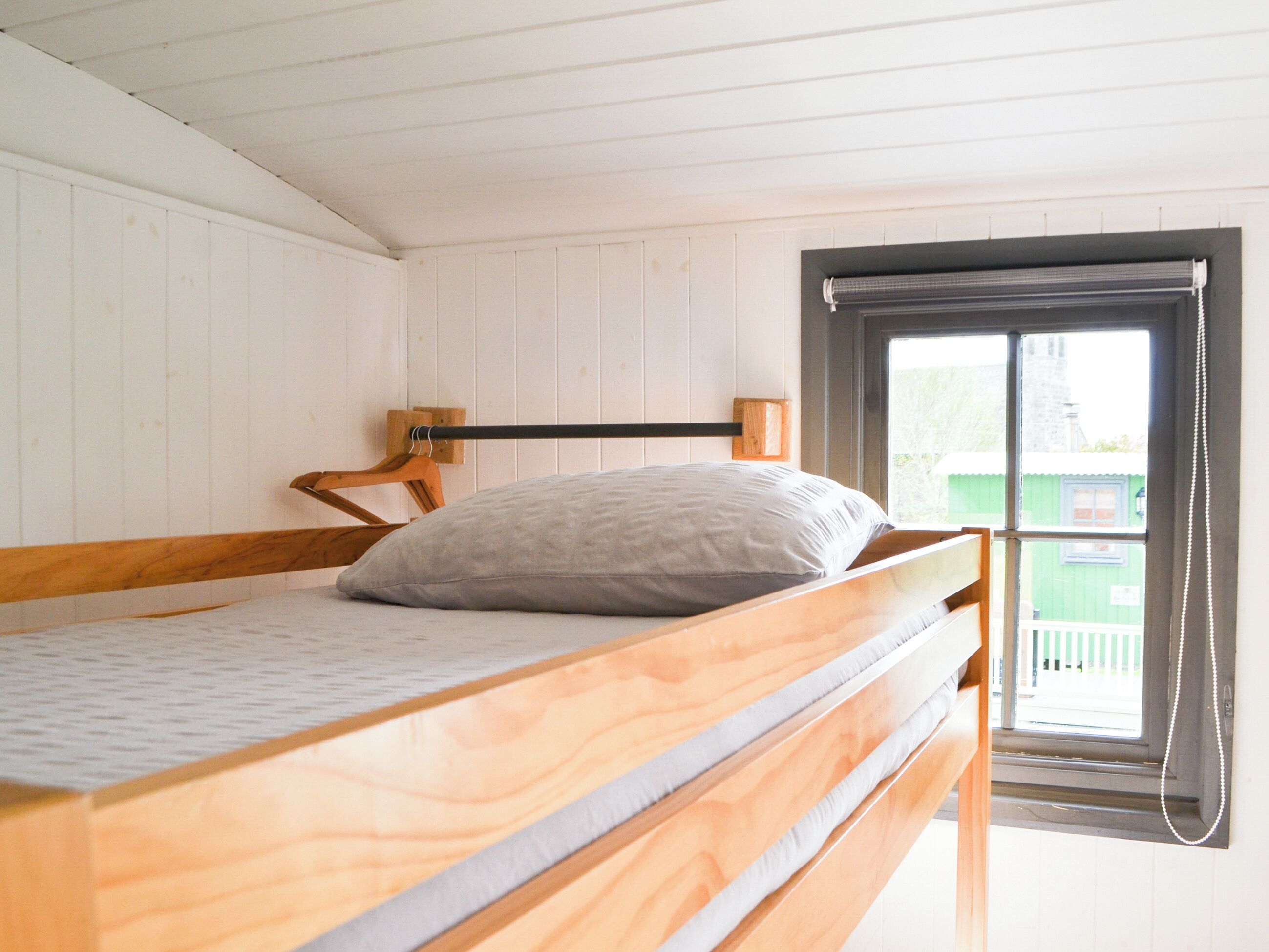 Een houten stapelbed met kussen, houten hoofdbord en raam met gordijn.