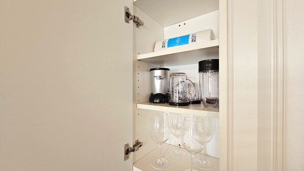 Un mueble de cocina con una licuadora, una cafetera y copas de vino.