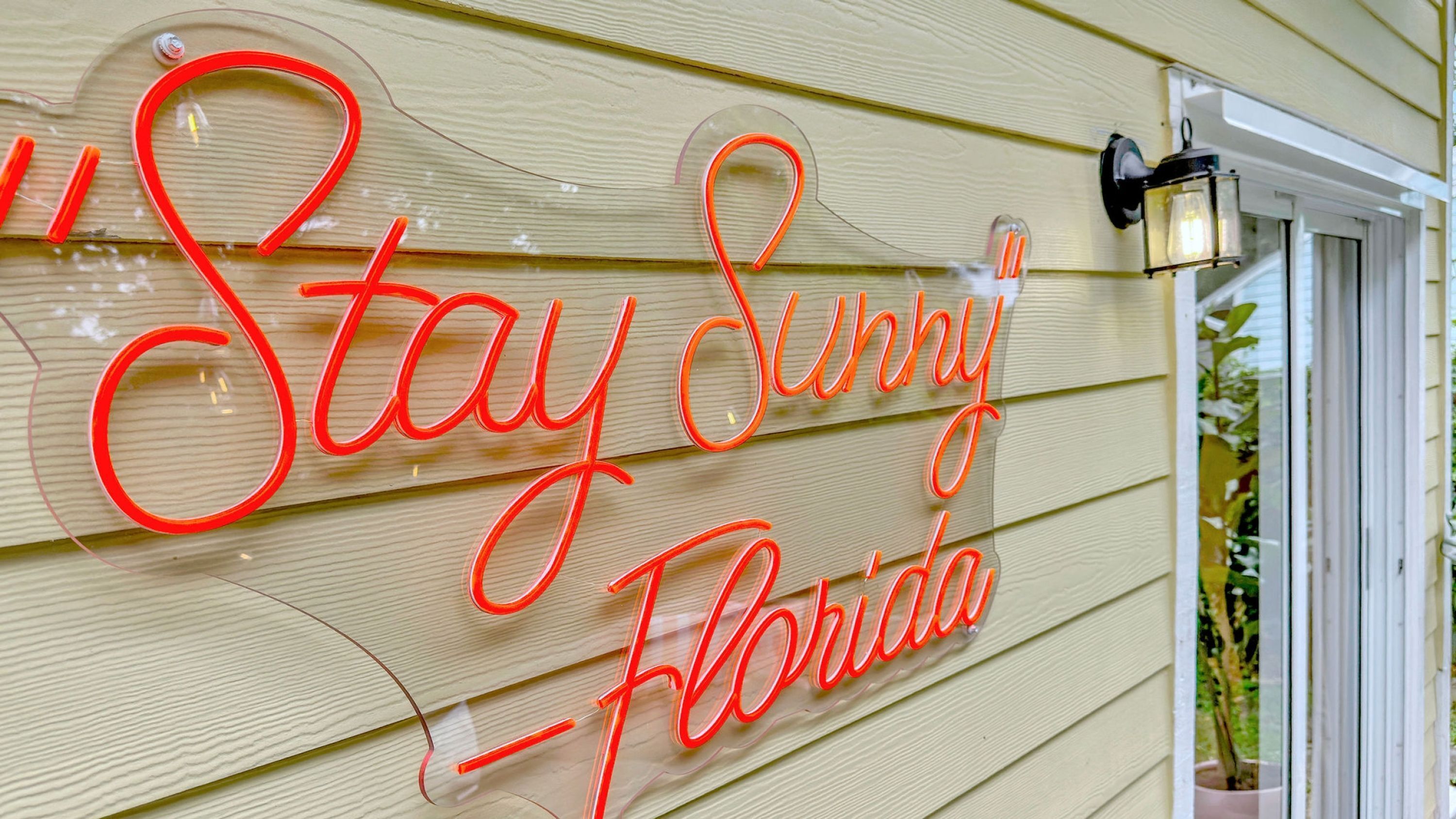 A neon sign on a building that reads "Stay Sunny Florida".