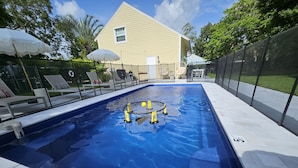 Piscina com rede de proteção, espreguiçadeiras e uma casa ao fundo.
