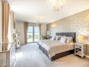A bedroom with a large bed, a chandelier, a nightstand, and a view through the glass doors.