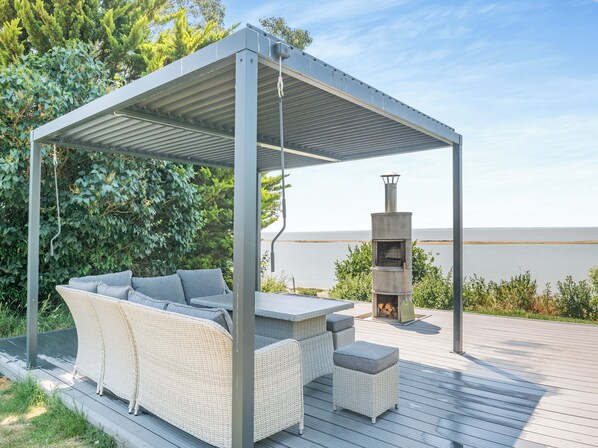 A covered outdoor seating area with a sofa and ottoman, a grill, and a view of the water.