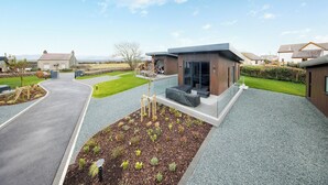 A modern building with a paved driveway, a landscaped garden, and a clear sky.