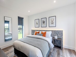 Une chambre à coucher moderne avec un grand lit, une table de chevet, un miroir et des reproductions encadrées de motifs botaniques accrochées au mur.