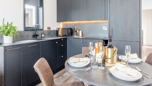 A modern kitchen with dark cabinetry, a built-in oven, and a dining area set for six with a round table and six chairs.