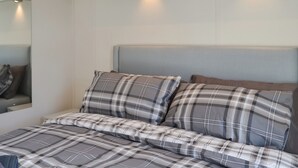 Un dormitorio con cama, almohadas, cabecero e iluminación en la pared.