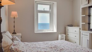 Un dormitorio con cama, mesita de noche, lámpara, cómoda y ventana con vista al mar.