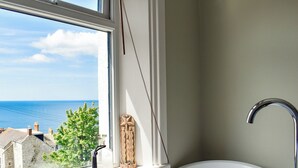 Un baño con bañera, una ventana que da al mar y un estante con objetos decorativos.