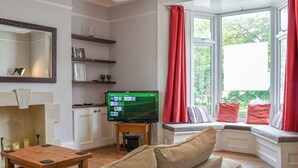 Una sala de estar con un sofá, una mesa de centro, un televisor y una ventana con cortinas rojas.