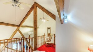 A bedroom with a wooden ceiling, a red carpet, a bed, a rocking chair, and a chandelier.