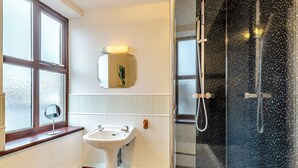 A bathroom with a pedestal sink, a mirror, a window with frosted glass, and a shower with a glass door.