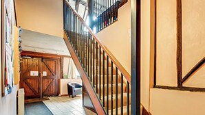 Un escalier avec des rampes en bois et un sol carrelé menant à une mezzanine dotée d’une grande porte en bois.