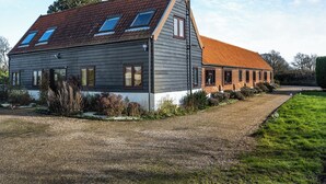 Une maison à deux étages, dotée d’un toit en pente, de grandes fenêtres et d’une allée gravillonnée.