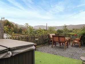 Eine Terrasse im Freien mit einem Holztisch und -stühlen, umgeben von einem Holzzaun und Blumentöpfen.