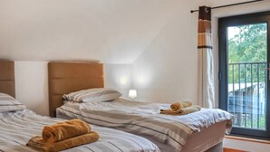 Ein Schlafzimmer mit zwei Betten, einem Fenster mit Blick auf Grünflächen und einer Wandleuchte.