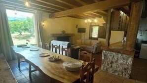 Un vaste espace de vie comprenant un coin repas avec une table en bois, un canapé et une cuisine dotée d’un plan de travail en pierre.