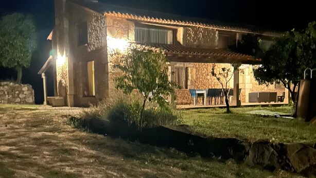 Un bâtiment en pierre avec un toit en tuiles, un escalier en pierre et un patio doté de sièges extérieurs.