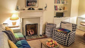 Una sala de estar acogedora con chimenea, un sillón a cuadros, un sofá con cojines de colores y una mesa de centro de madera con fruta.