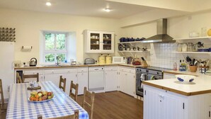 Una cocina con armarios blancos, una mesa de comedor con mantel a cuadros y diferentes electrodomésticos.