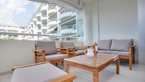 Un balcon avec des meubles en bois, un pichet blanc et une bouteille d’alcool.