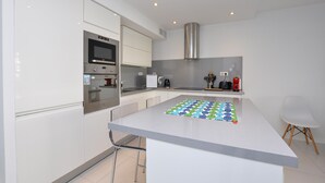 Une cuisine moderne avec des meubles blancs, un four en acier inoxydable, un micro-ondes encastré et un grand îlot central agrémenté d’un set de table coloré.
