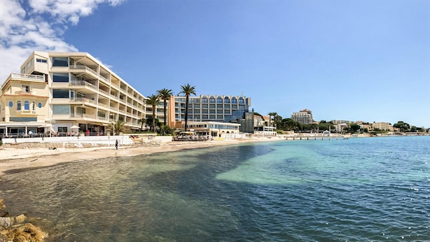 Un hôtel situé sur la côte, doté de nombreux balcons, bénéficiant d’un emplacement en bord de plage et offrant une vue sur une eau d’un bleu limpide.