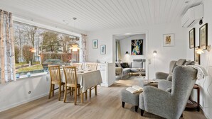 Ein modernes Wohnzimmer mit Essbereich, ausgestattet mit einem großen Fenster, Holzböden und zeitgemäßer Möbel.