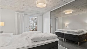 Ein modernes Schlafzimmer mit einem großen Bett, einem Spiegel und Blick ins Freie.