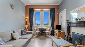 A cozy living room with a sofa, a dining table with chairs, a fireplace, and a television. - Top Floor Spacious King Size Apartment | City Views | Excellent Transport Links (Edinburgh)
