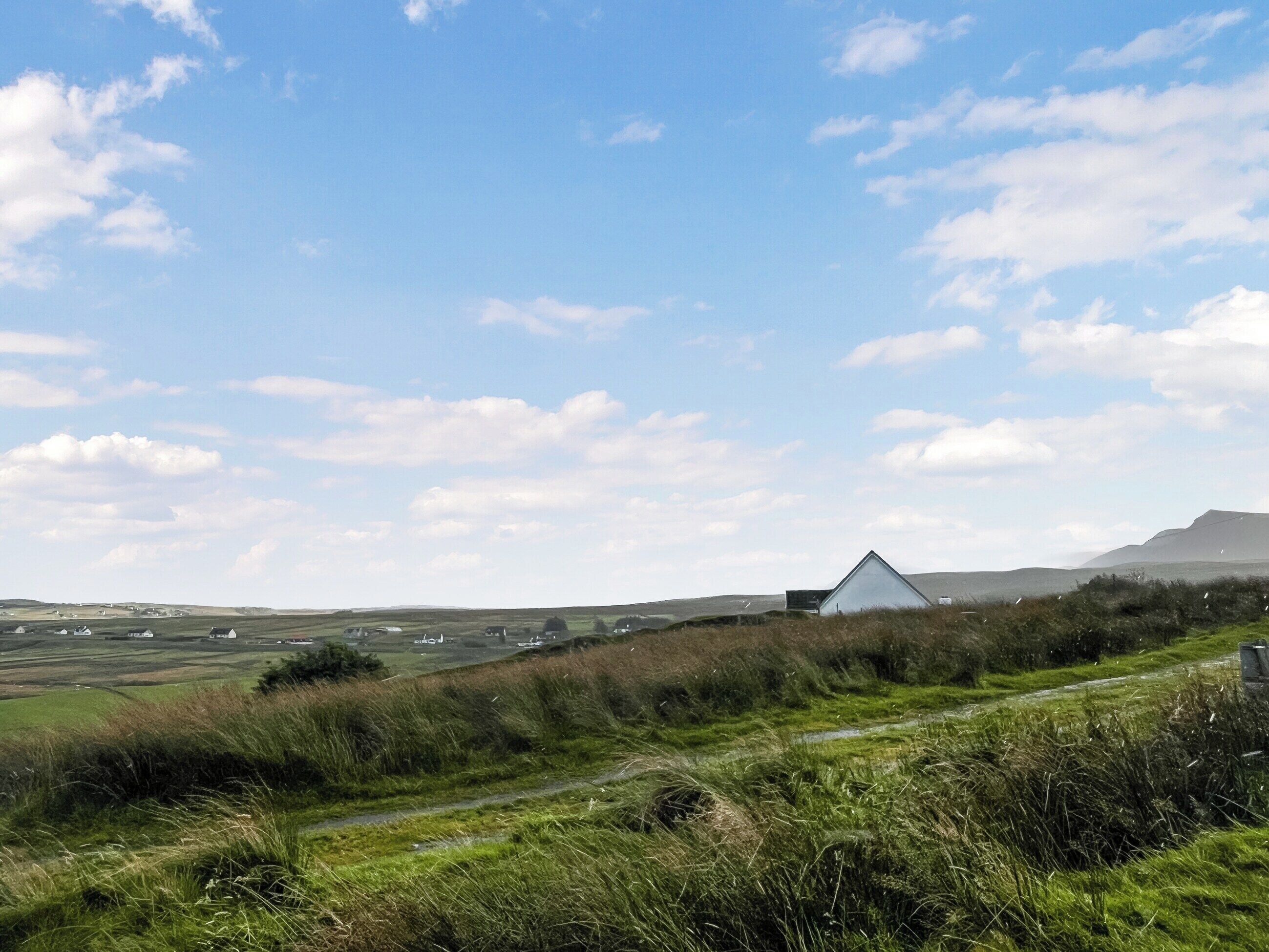 A rural landscape with a prominent white building on a hill, surrounded by fields and a clear sky.