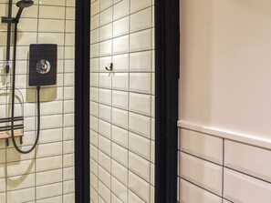 A bathroom with a tiled wall, a shower area, and a black-framed mirror.