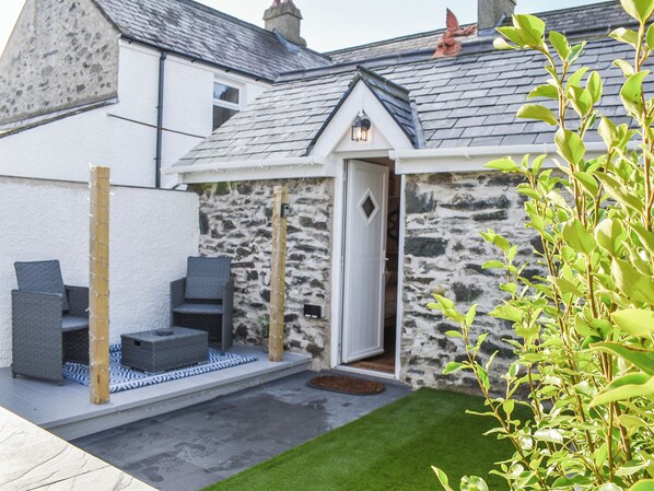 A stone house with a door, a small porch with seating, and a grassy yard.