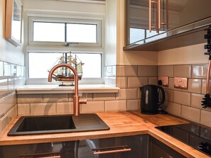 A kitchen with a window, a sink, a kettle, and a stove.
