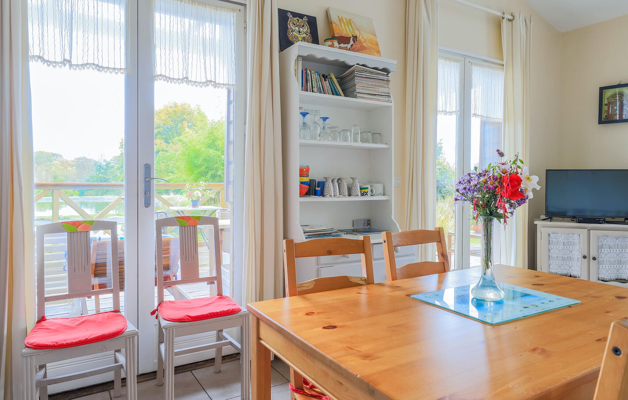 A dining area with a wooden table, chairs, a bookshelf, and a television.