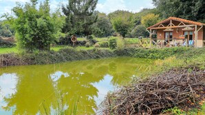 A rustic wooden cabin with a tiled roof, surrounded by lush greenery and a pond. - Amazing home in Gueschart with house sea view (Gueschart)