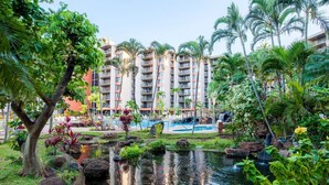 A hotel with a pool, lush greenery, and a pond.