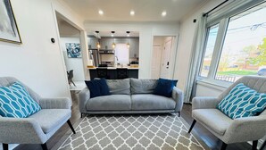 Ein modernes Wohnzimmer mit einem grauen Sofa, passenden Sesseln und einem gemusterten Teppich.