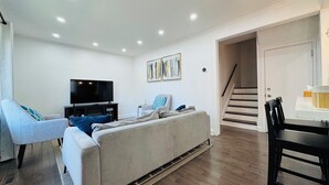 Ein modernes Wohnzimmer mit einer Couch, einem Fernseher und einer Treppe zu einem weiteren Raum.
