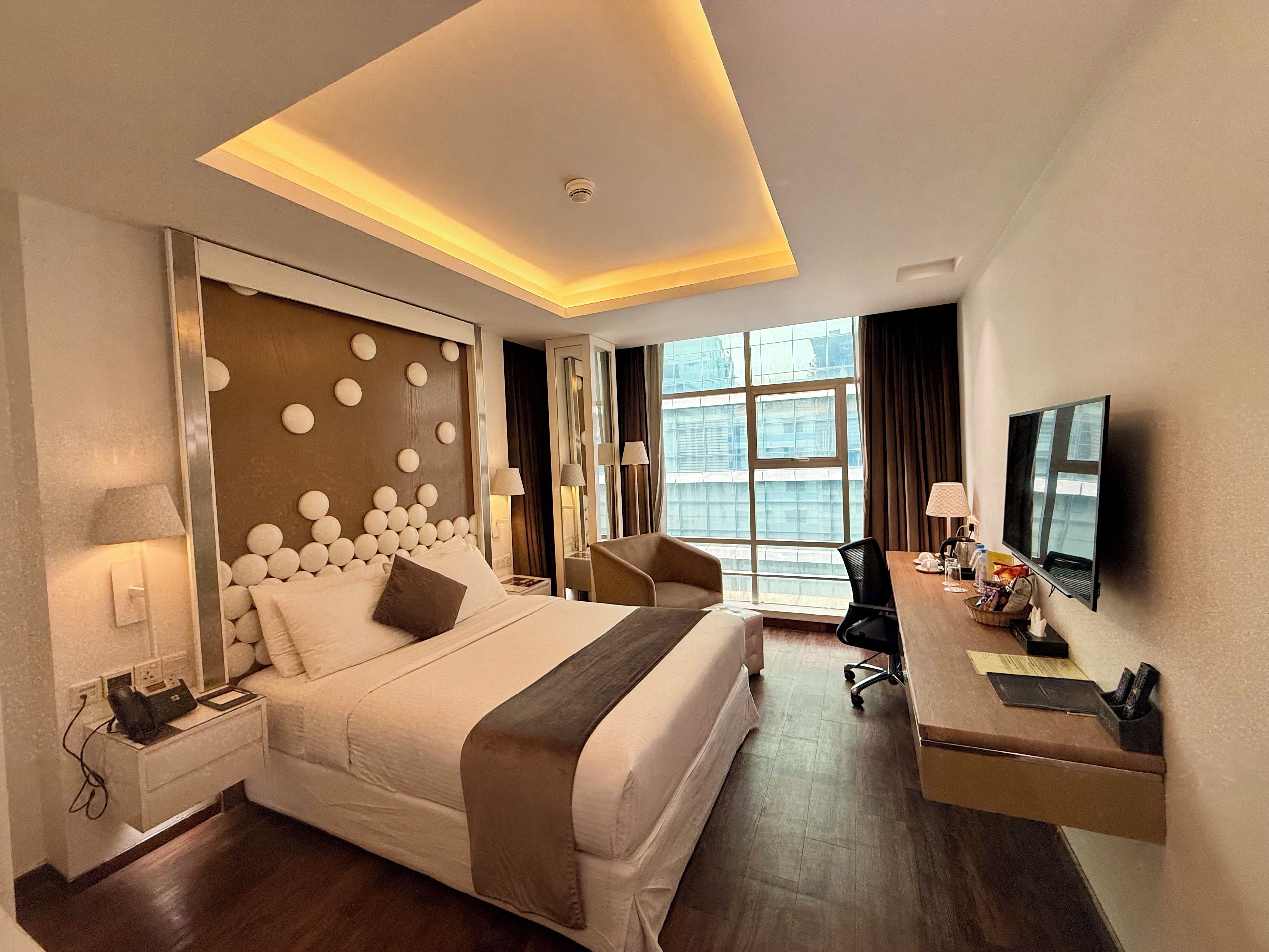 A hotel room with a large bed, a desk, a chair, a TV, and a window with a view.