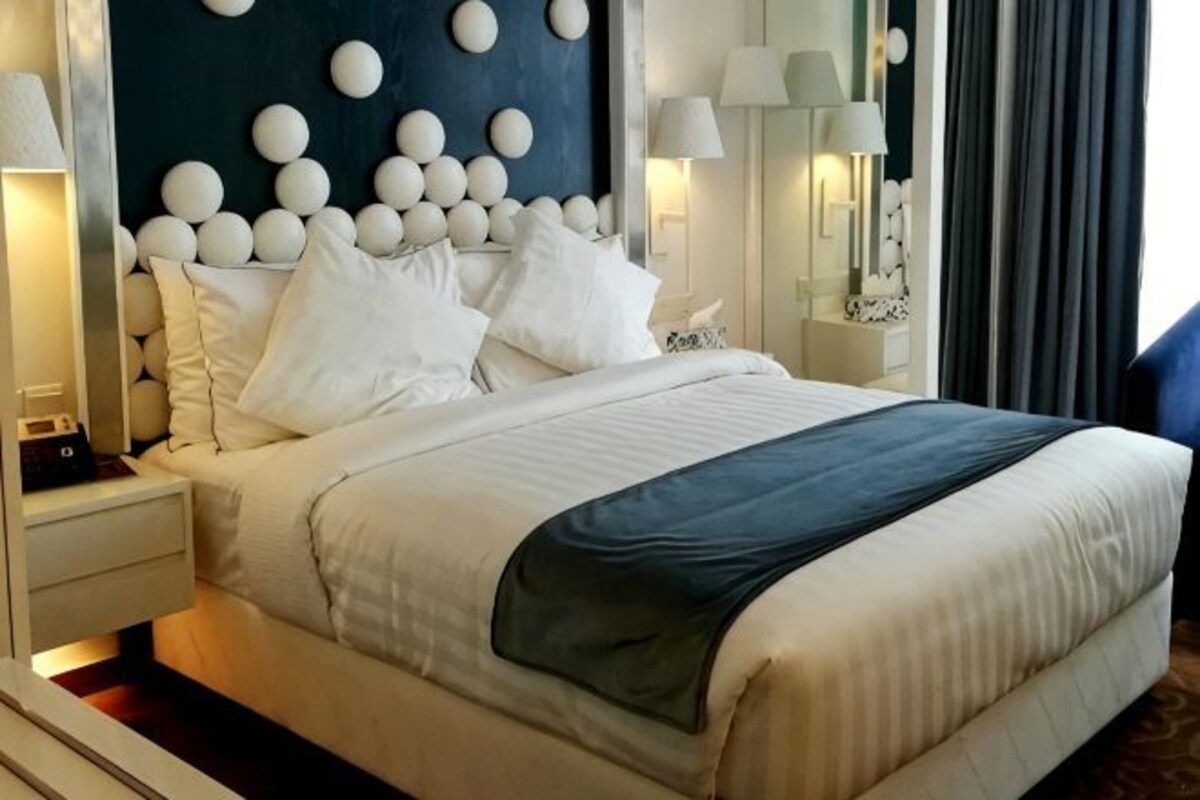 A hotel room with a large bed, white bedding, a dark headboard, and wall-mounted lamps.