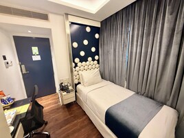 A hotel room with a bed, a desk, a chair, a nightstand, a phone, and a door.
