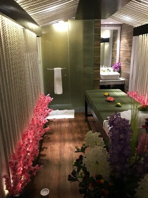 A spa room with a wooden floor, a green wall, a white towel hanging on a rack, a sink, and a bed with flowers. - Grace 21 Smart Hotel (Dhaka)