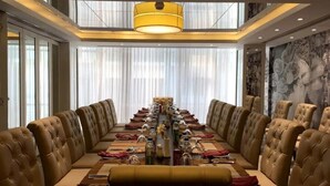 A long dining table with multiple chairs, a chandelier, and a view of the city through large windows. - Hotel Grace 21 (Dhaka)