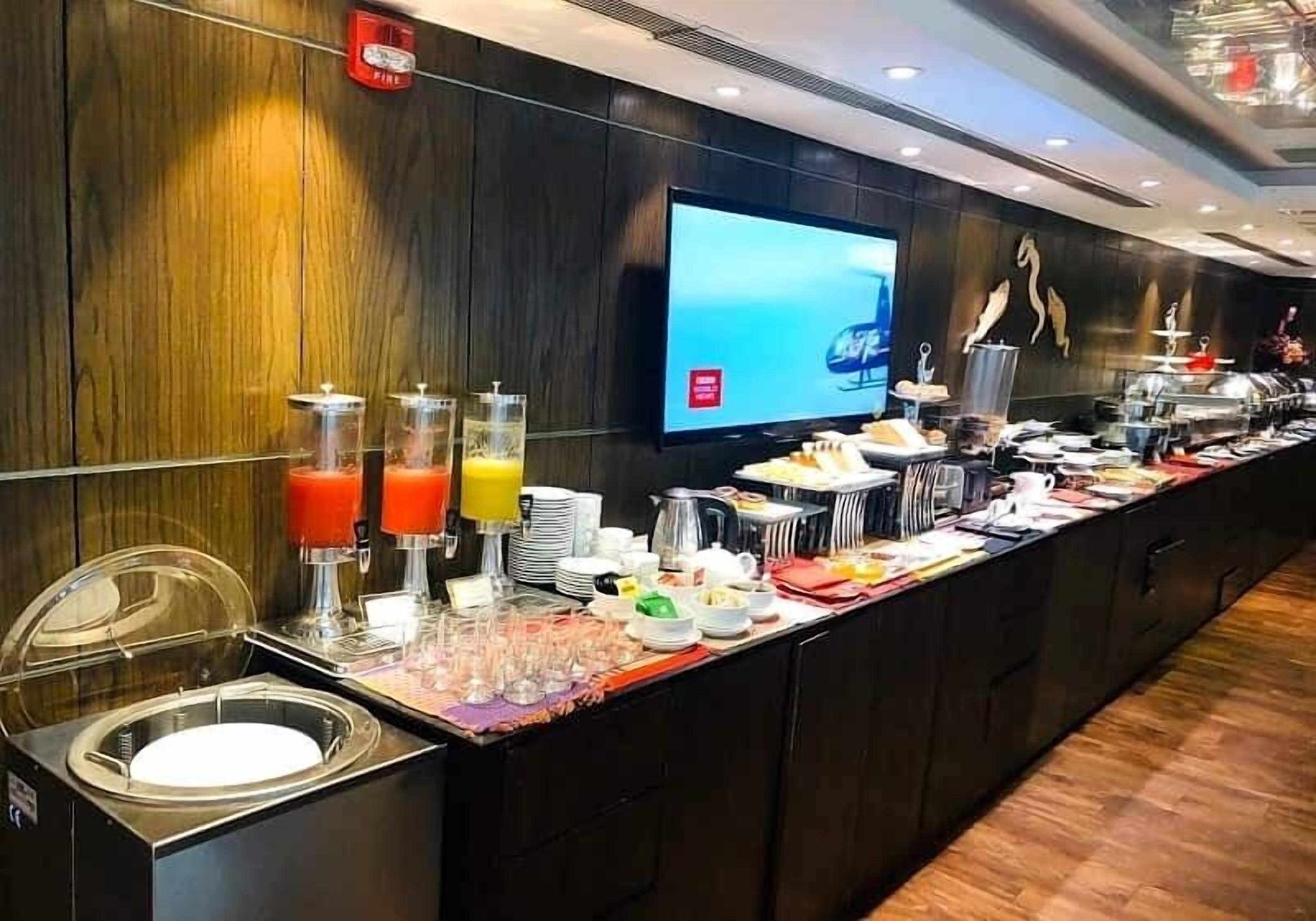 Disposición de buffet con diversos alimentos y bebidas, una pantalla de televisión y un detector de incendios en la pared.